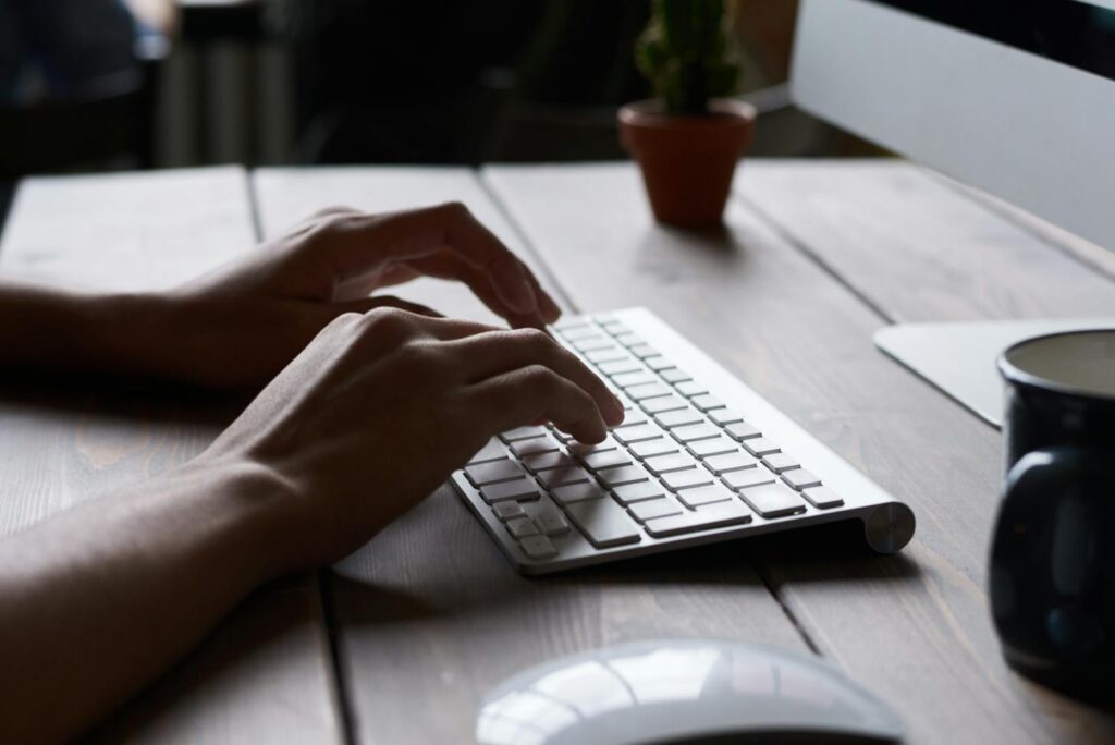 Close-up of hands typing on a wireless keyboard at a modern workspace.