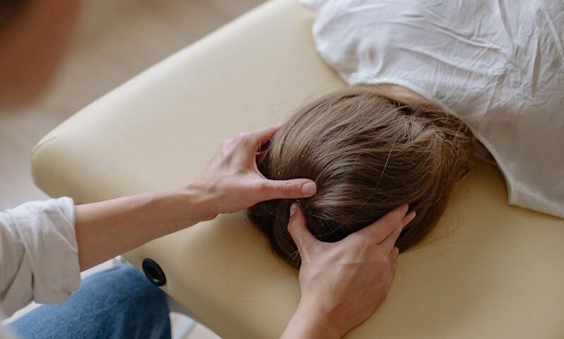 A chiropractor performing a therapeutic head massage on a woman lying on a massage table.