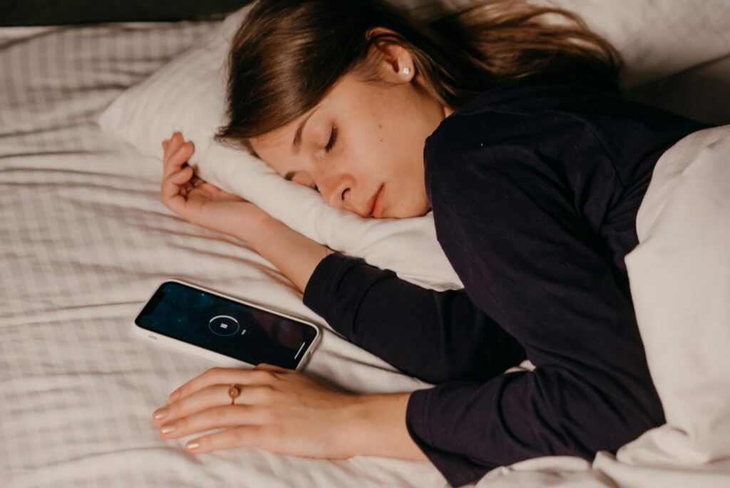 A woman peacefully sleeping in bed with a smartphone nearby, conveying rest and relaxation.
