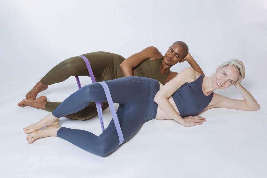 Two diverse women in activewear stretching with resistance bands during a studio workout session.