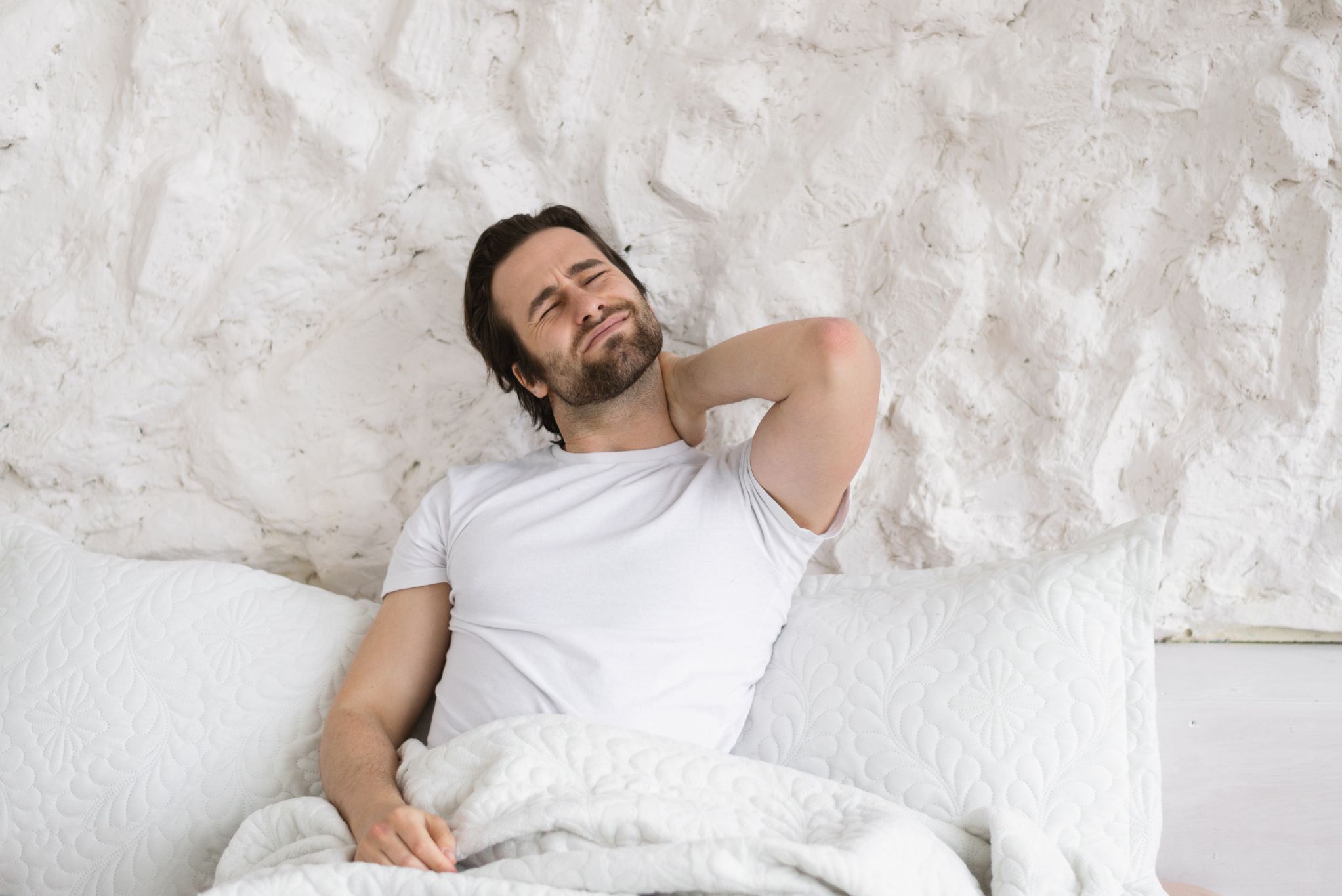 Man waking up with a stiff neck, possibly due to a poor sleeping posture or bad pillow.