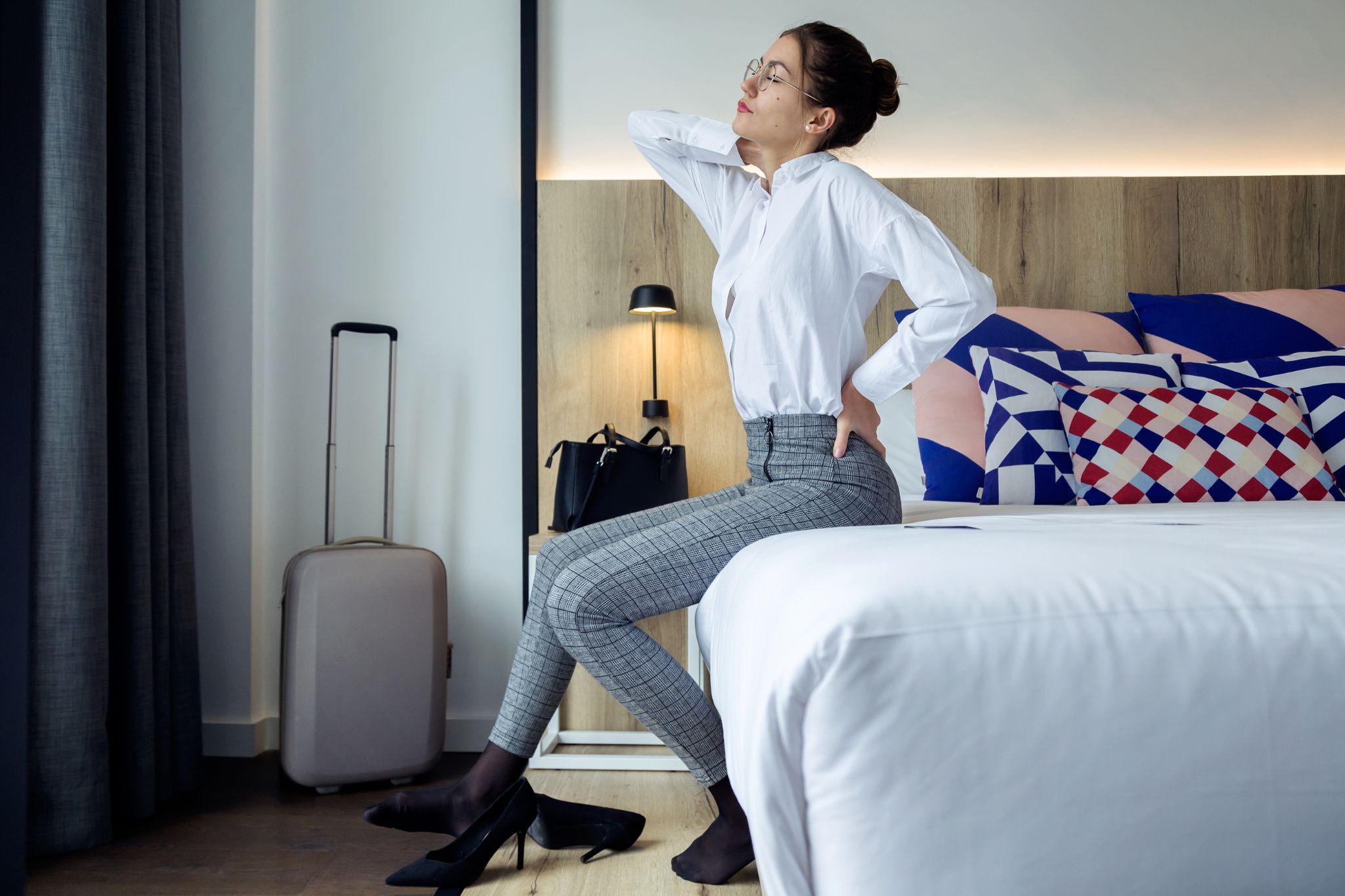 Female traveler experiencing back and neck pain in her hotel room after a long business trip.
