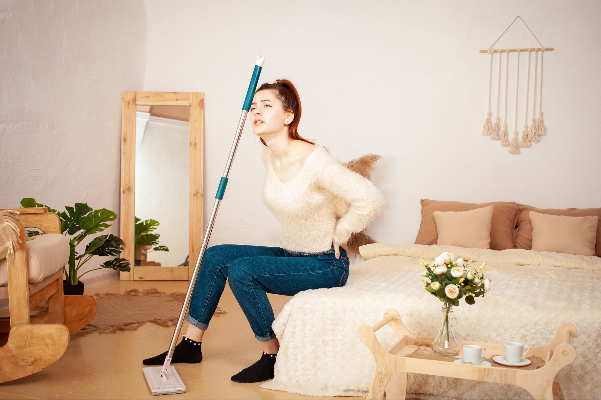 Woman resting on a bed after cleaning, experiencing back discomfort.