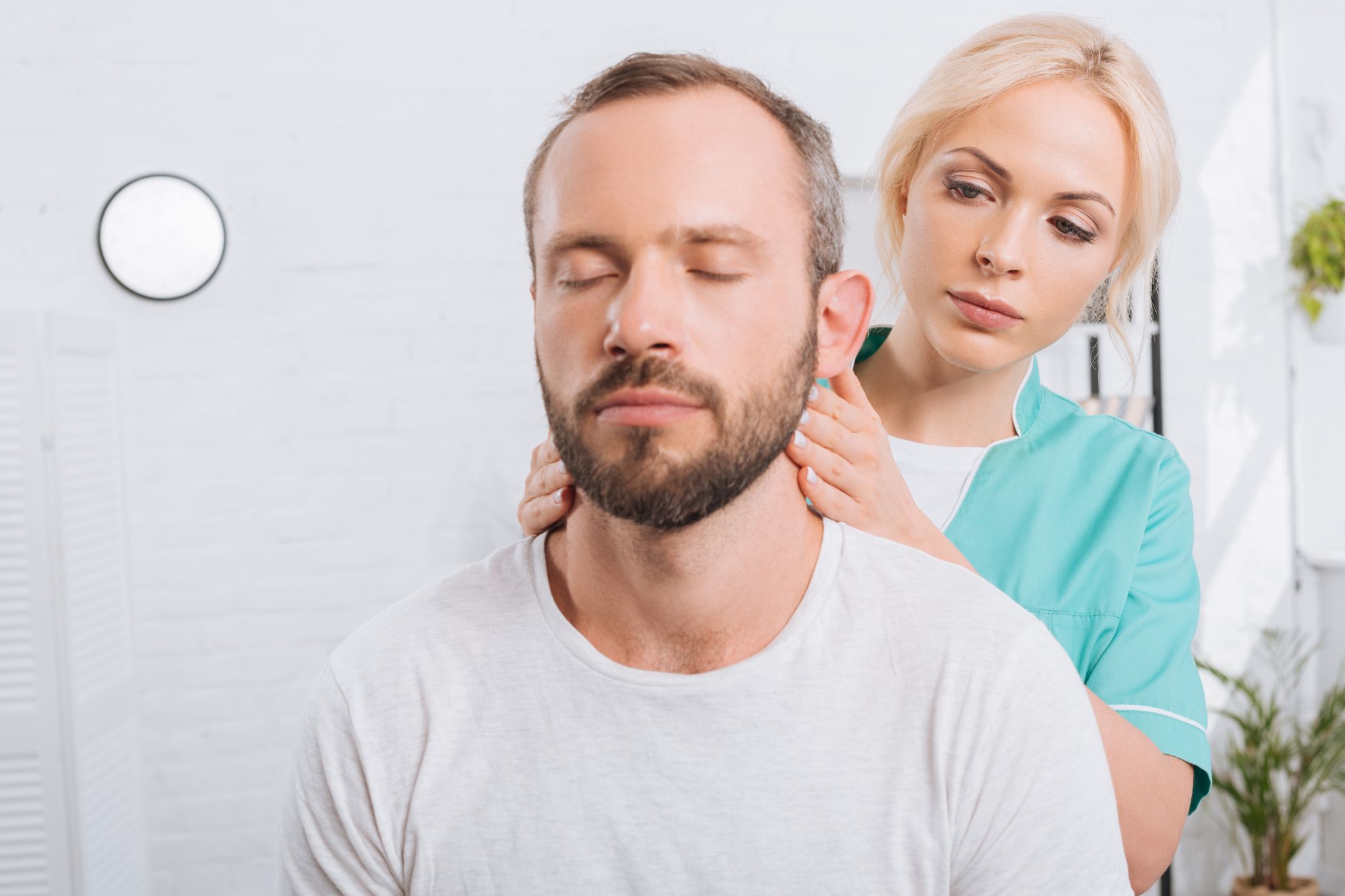 A healthcare professional is gently examining or massaging a man’s neck and upper shoulders. The man has his eyes closed, appearing relaxed, while the practitioner focuses carefully on the treatment.