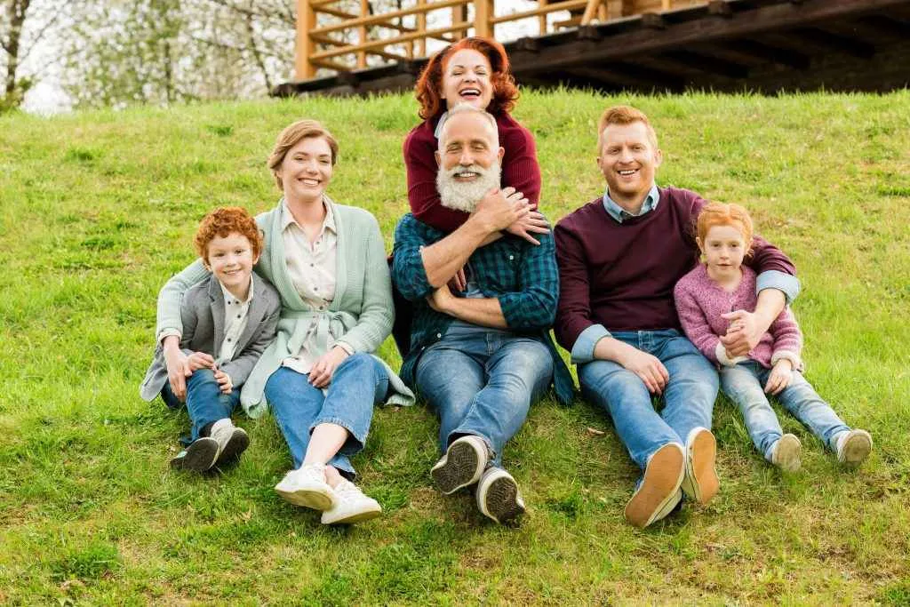 A happy multigenerational family sitting together on a grassy hill, smiling and enjoying time outdoors.