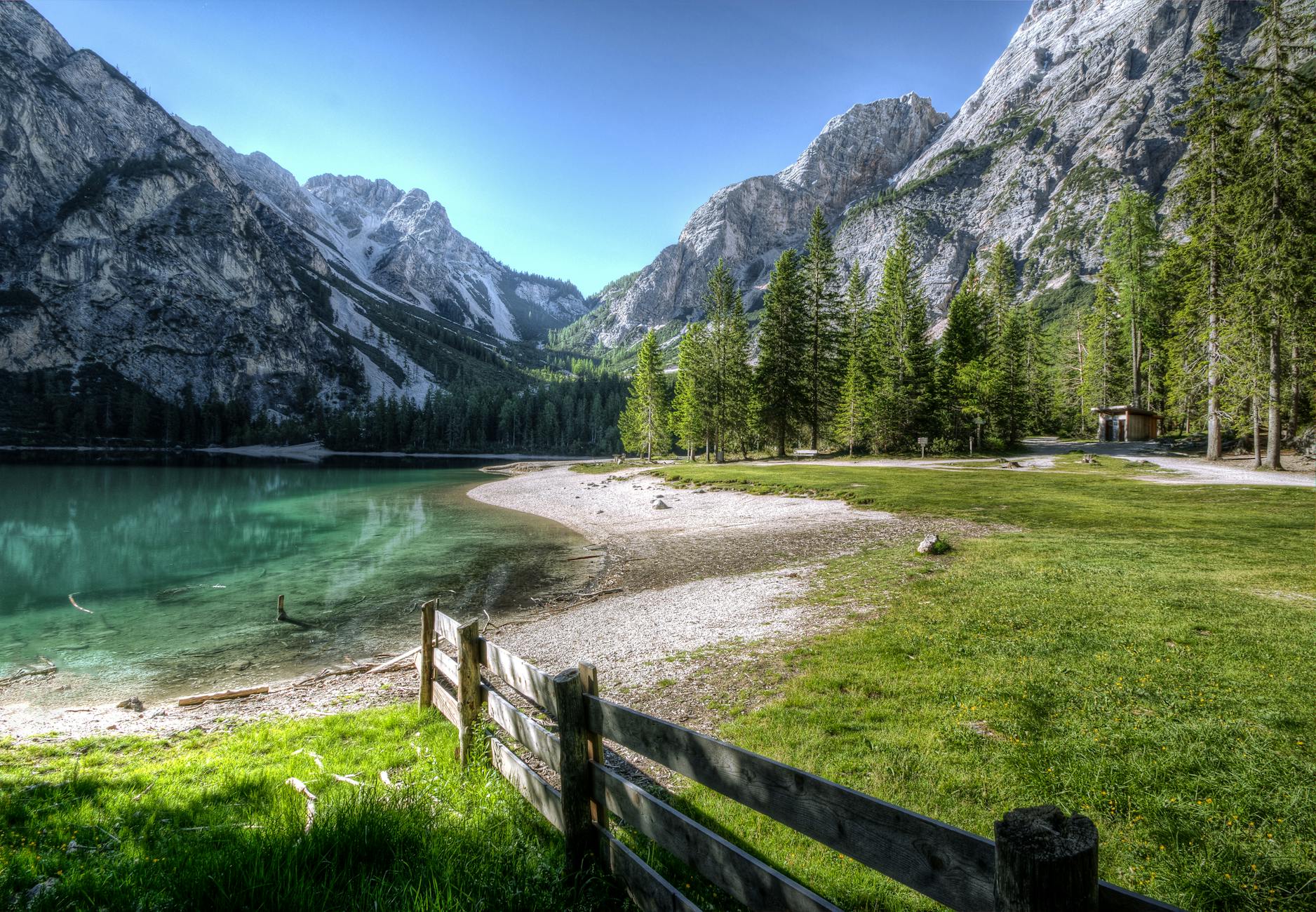 Serene mountain lake with green trees and a rustic fence, perfect nature backdrop.
