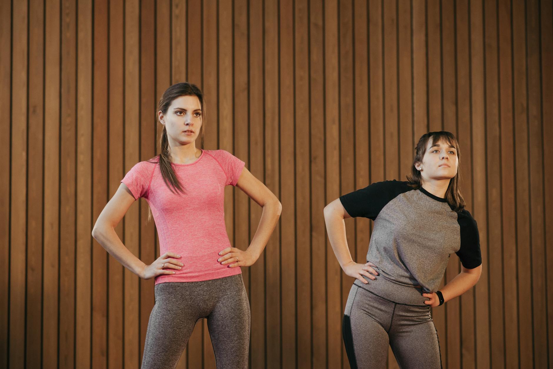 Two women wearing activewear performing stretching exercises indoors.